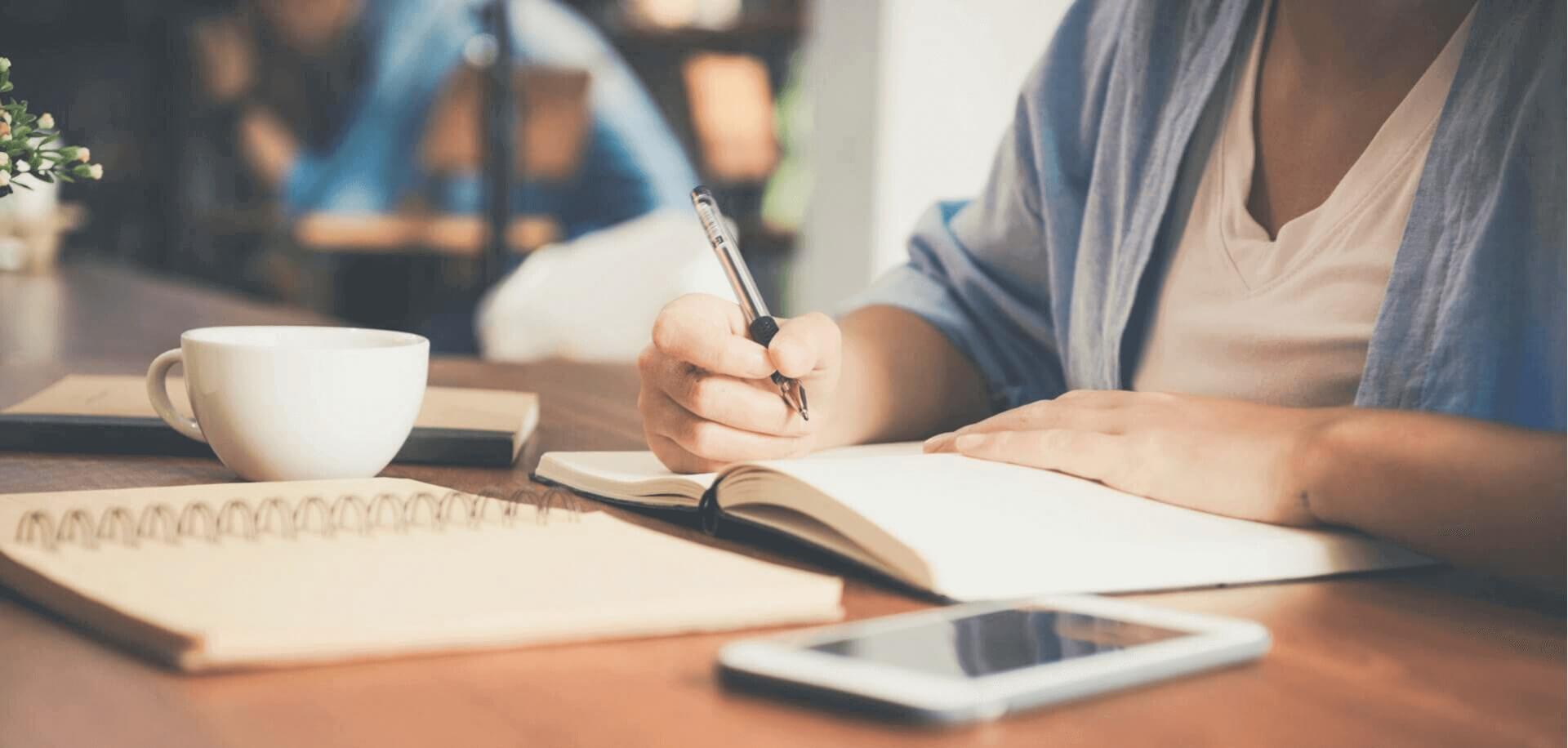 A person sitting in front of a desk writing on a notebook.